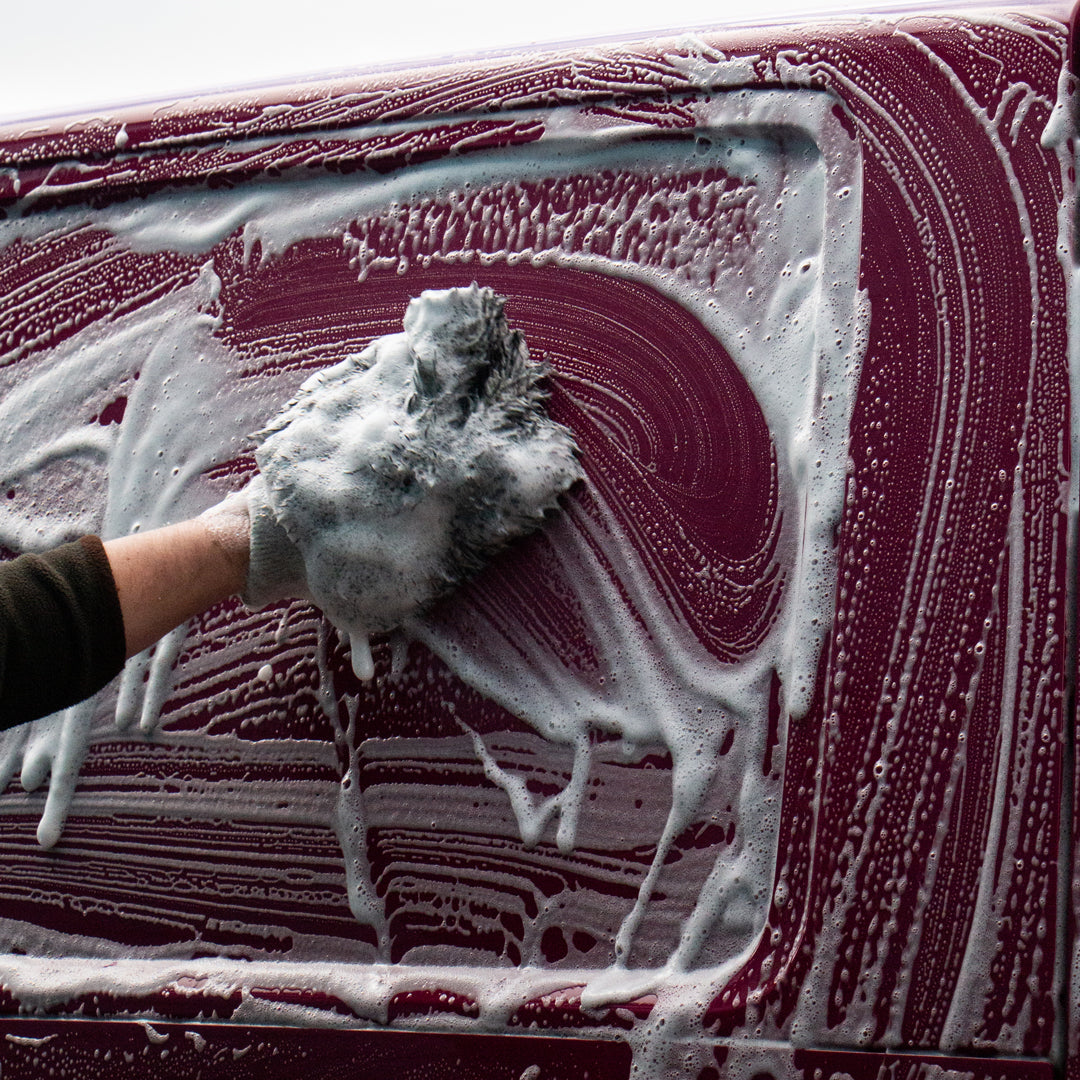 Person cleaning a car with a soapy sponge